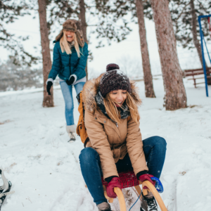 Two friends having a blast sledding in the snow, embracing the winter fun in Marshfield, WI, and Central Wisconsin's scenic winter wonderland.